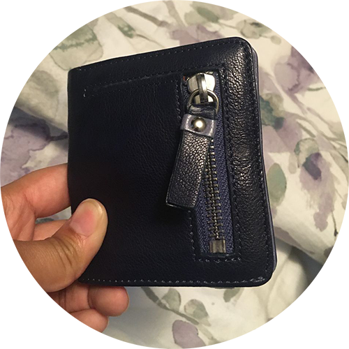 Hand holding a closed navy wallet with a prominent zipper pull.