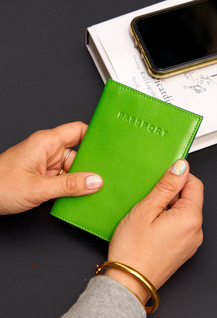 Hands holding a bright green passport cover over a table with a phone and book