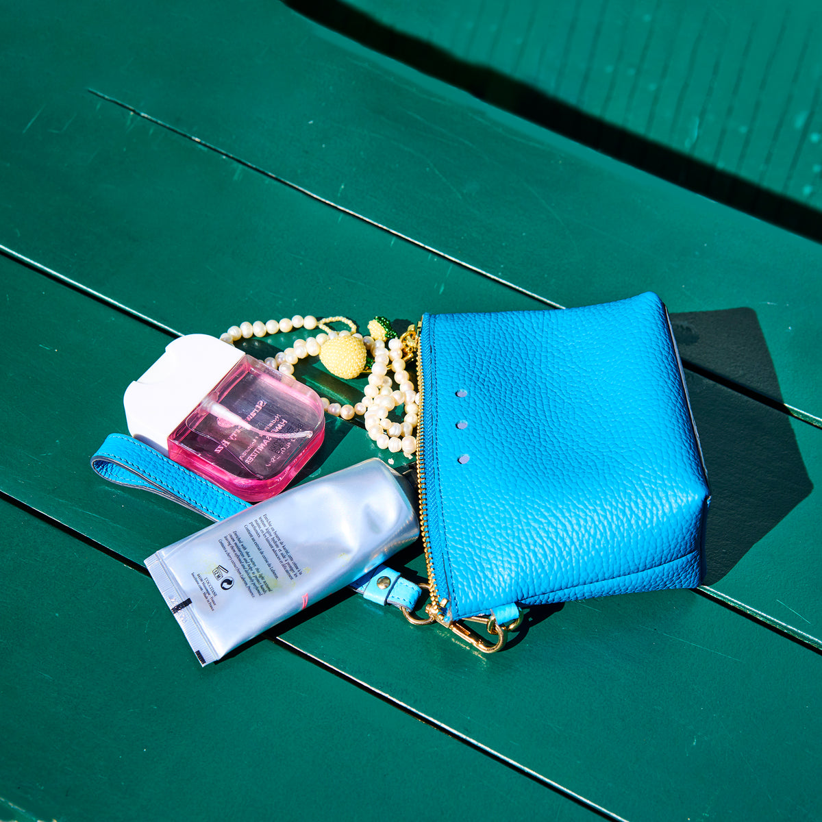 Blue handbag with skincare products on a green surface - AZURE