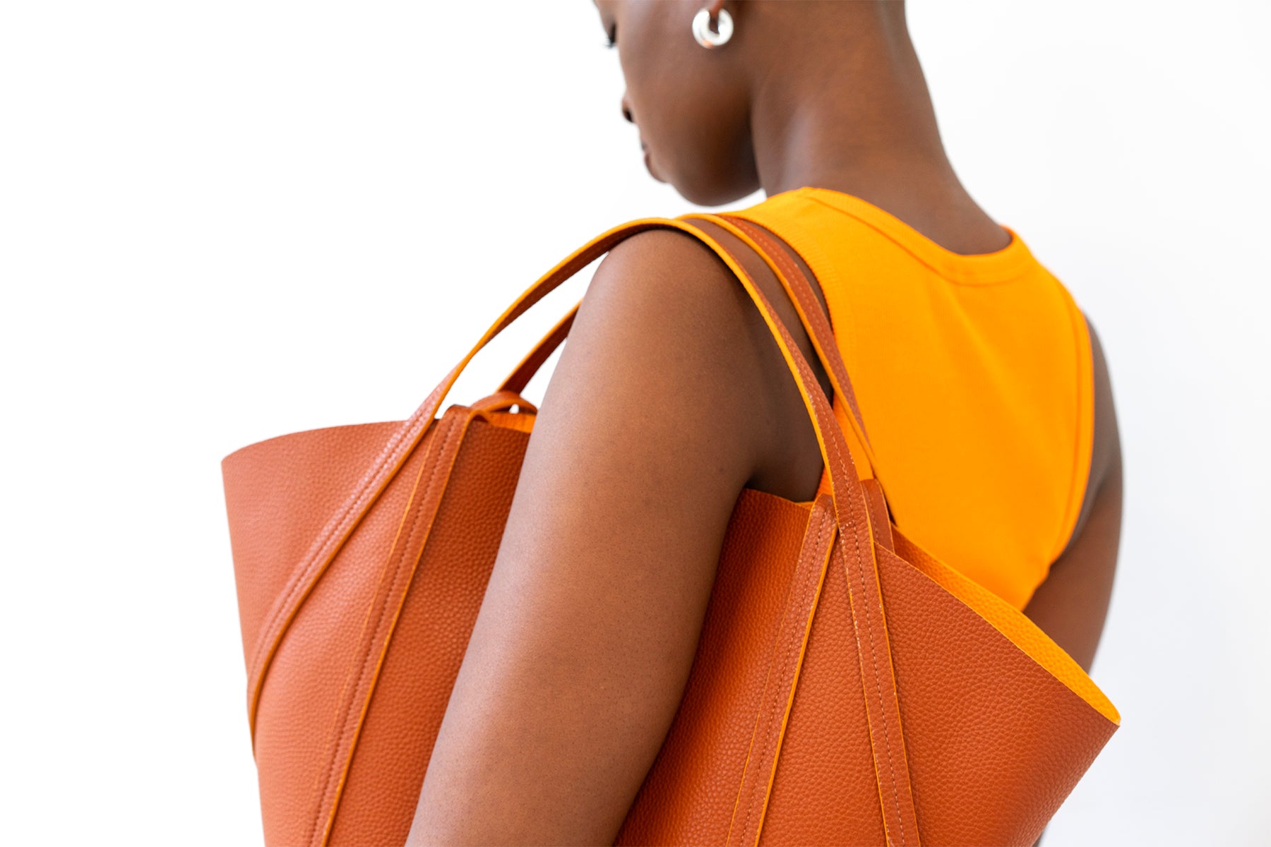 Woman in orange top carrying large tan tote bag with orange interior over shoulder.