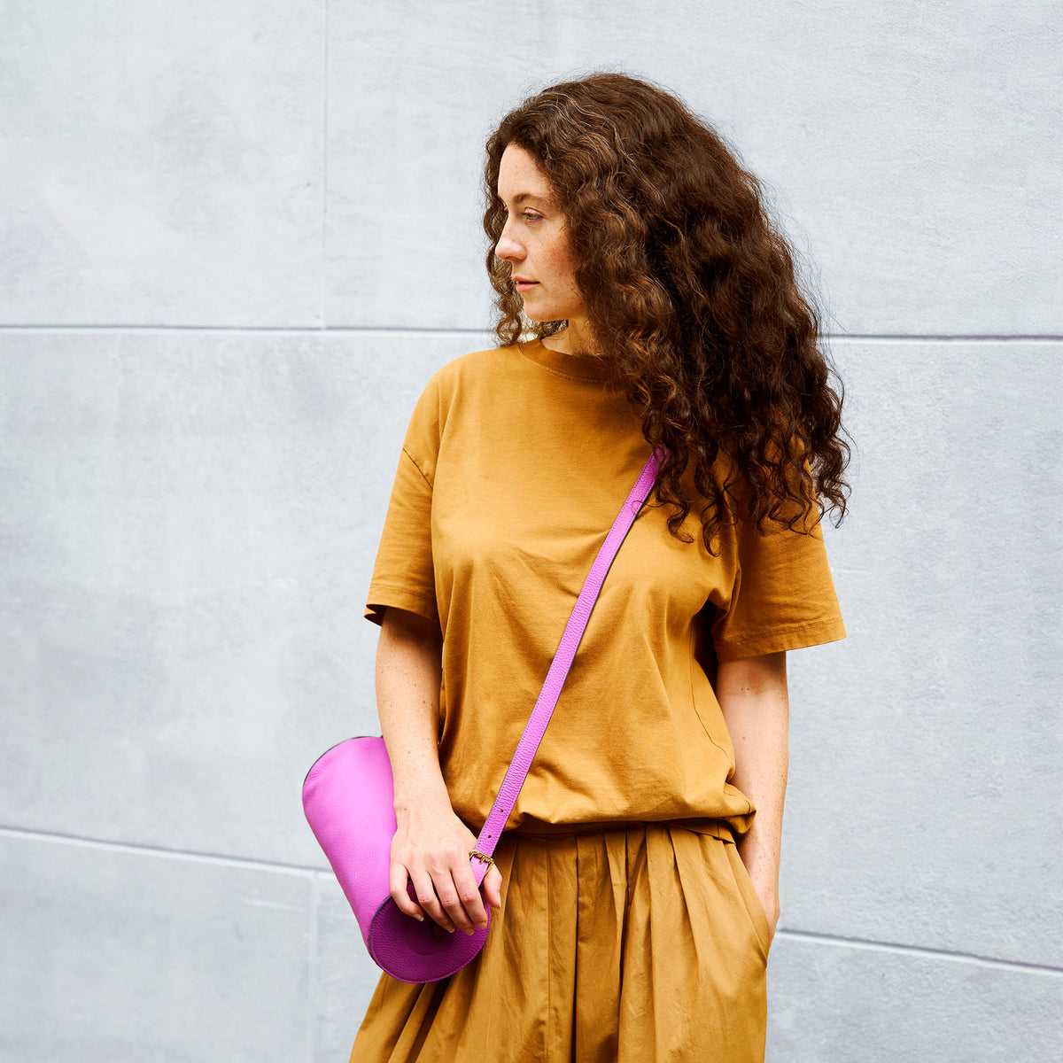 Woman holding a magenta leather bag against a gray wall - MAGENTA