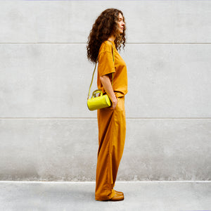 Woman in mustard yellow outfit holding a yellow leather handbag against a gray wall - LIME