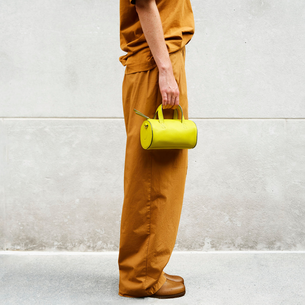 Person holding a yellow leather handbag in her hand against a light gray wall - LIME