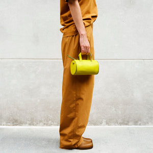 Person holding a yellow leather handbag in her hand against a light gray wall - LIME