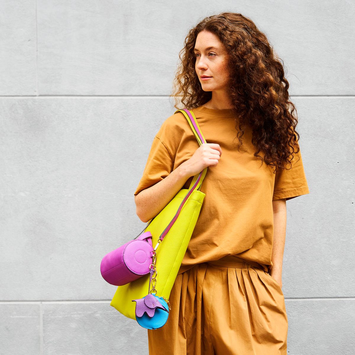 Woman holding a colorful leather bag against a gray wall - MAGENTA