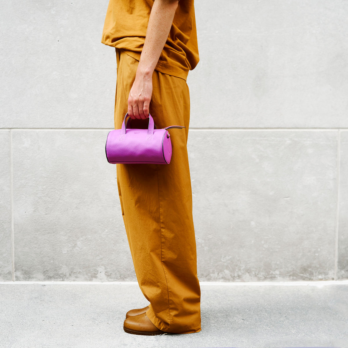 Person holding a magenta handbag against a light gray wall - MAGENTA