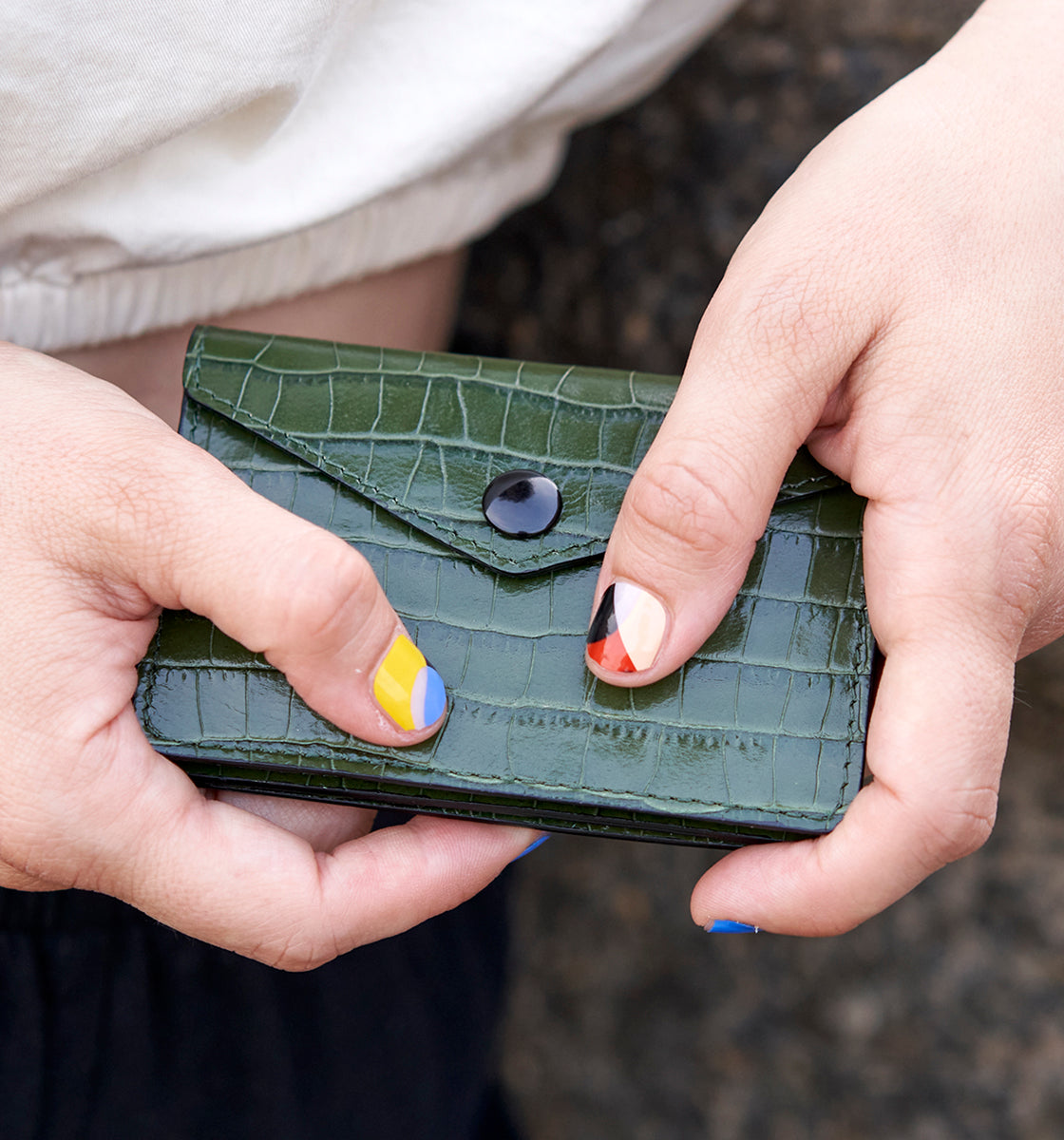 woman hands holding a small green textured wallet with a button closure.