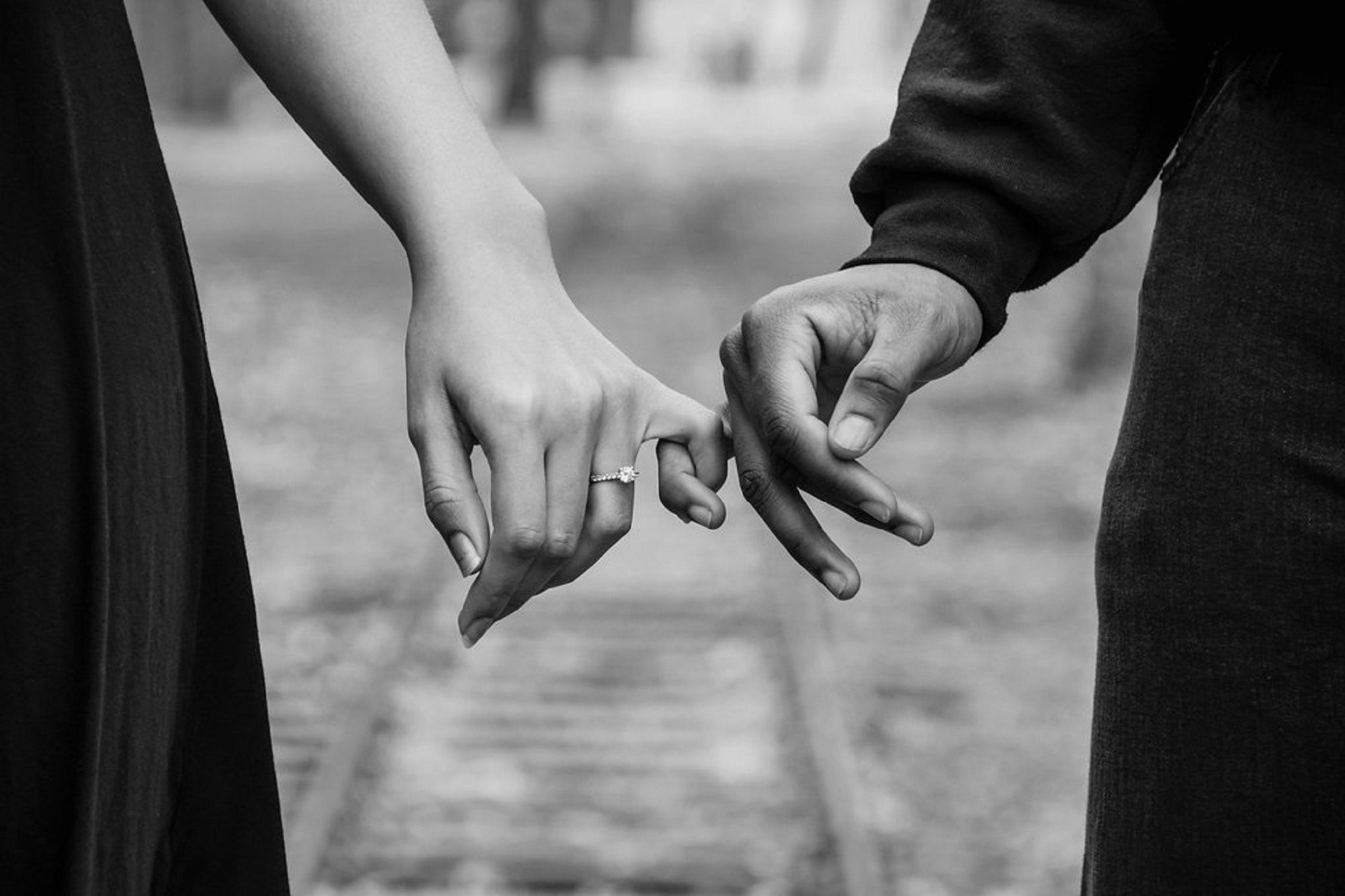 Close-up of a couple's hands gently touching fingertips in black and white.
