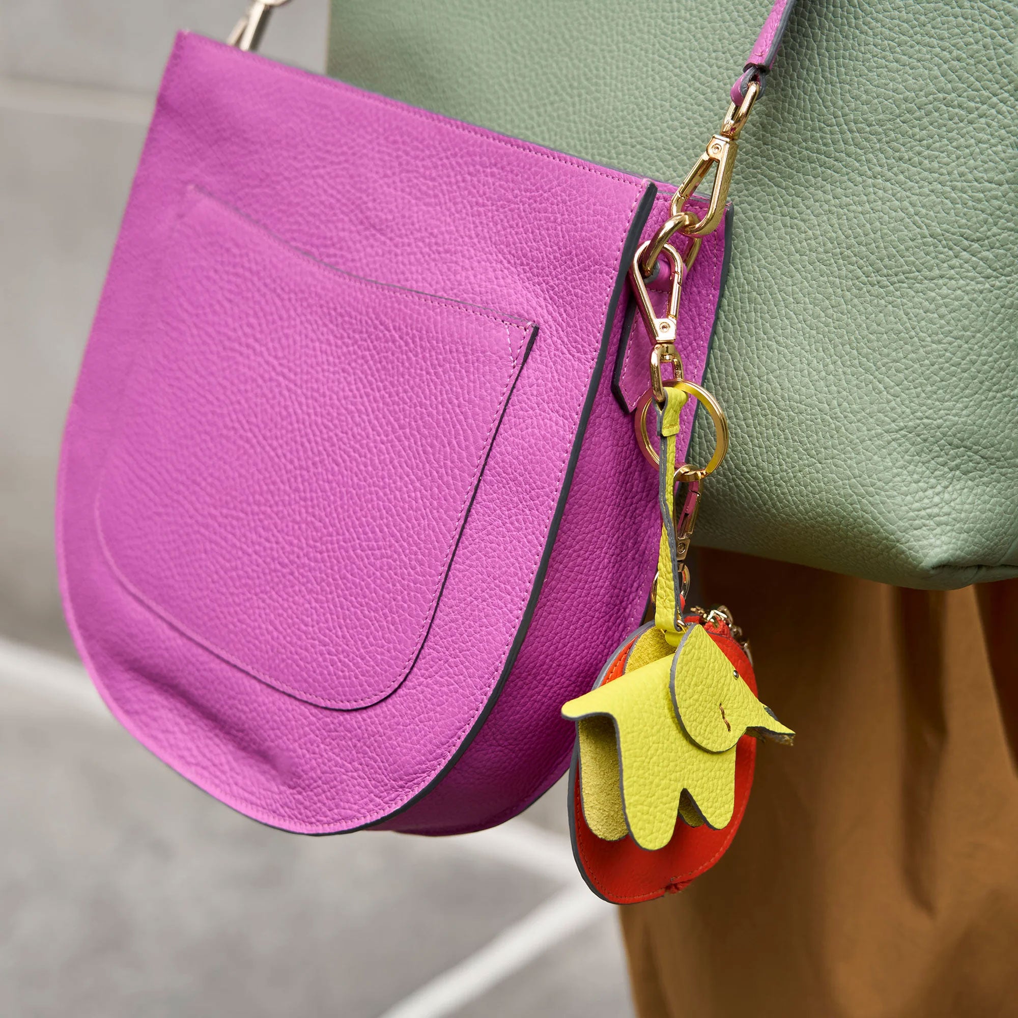 A vibrant purple handbag adorned with a colorful leather charm in green and red tones, resting against a neutral background.
