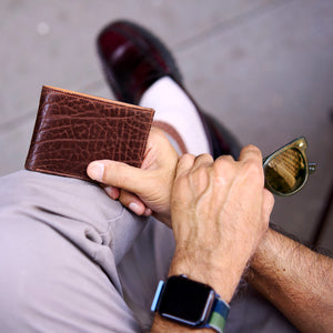 Person holding a brown leather wallet with sunglasses in hand - CHOCOLATE