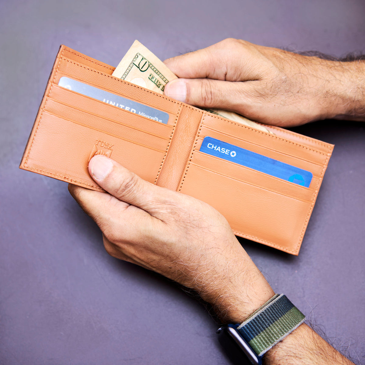 Person holding a brown leather wallet with cards and money on a purple background - CHOCOLATE