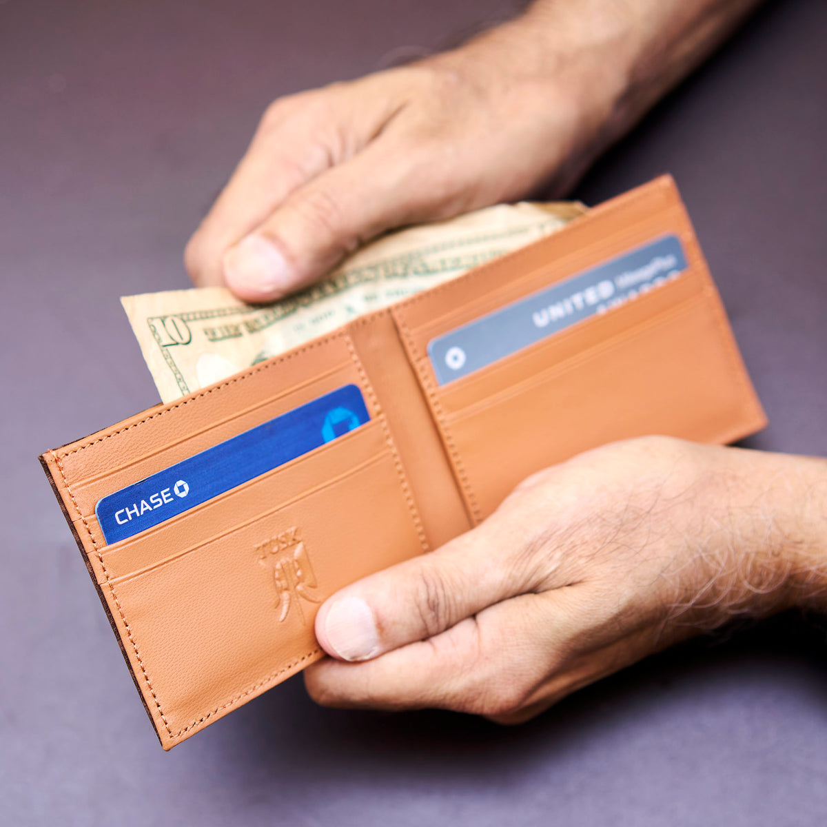 Brown leather wallet with cards and money held by a hand on a purple background - CHOCOLATE