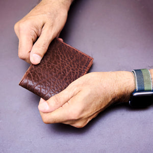 Brown leather wallet held by a person's hands on a purple background - CHOCOLATE