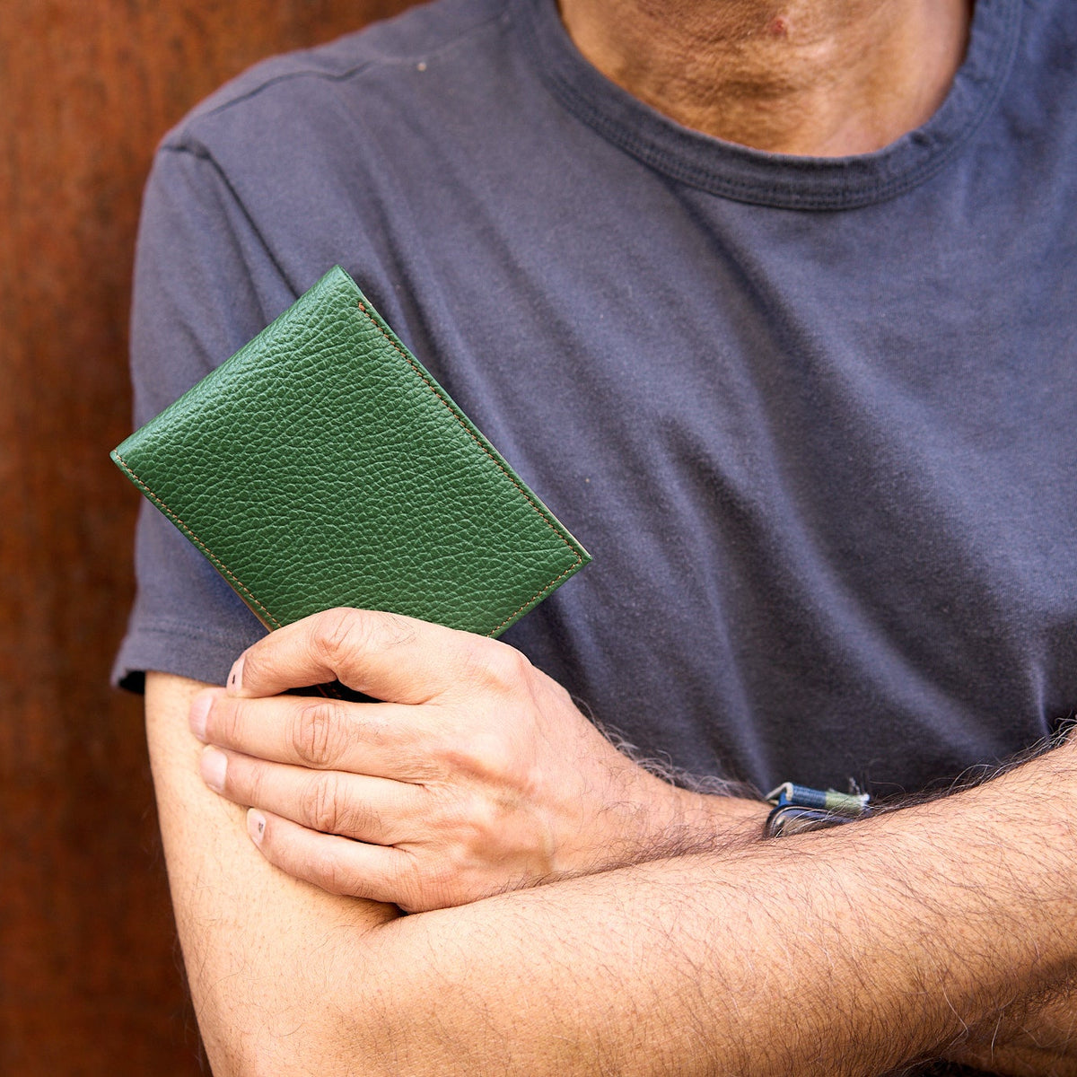 Man with folded arms holding green pebble grain billfold - FOREST