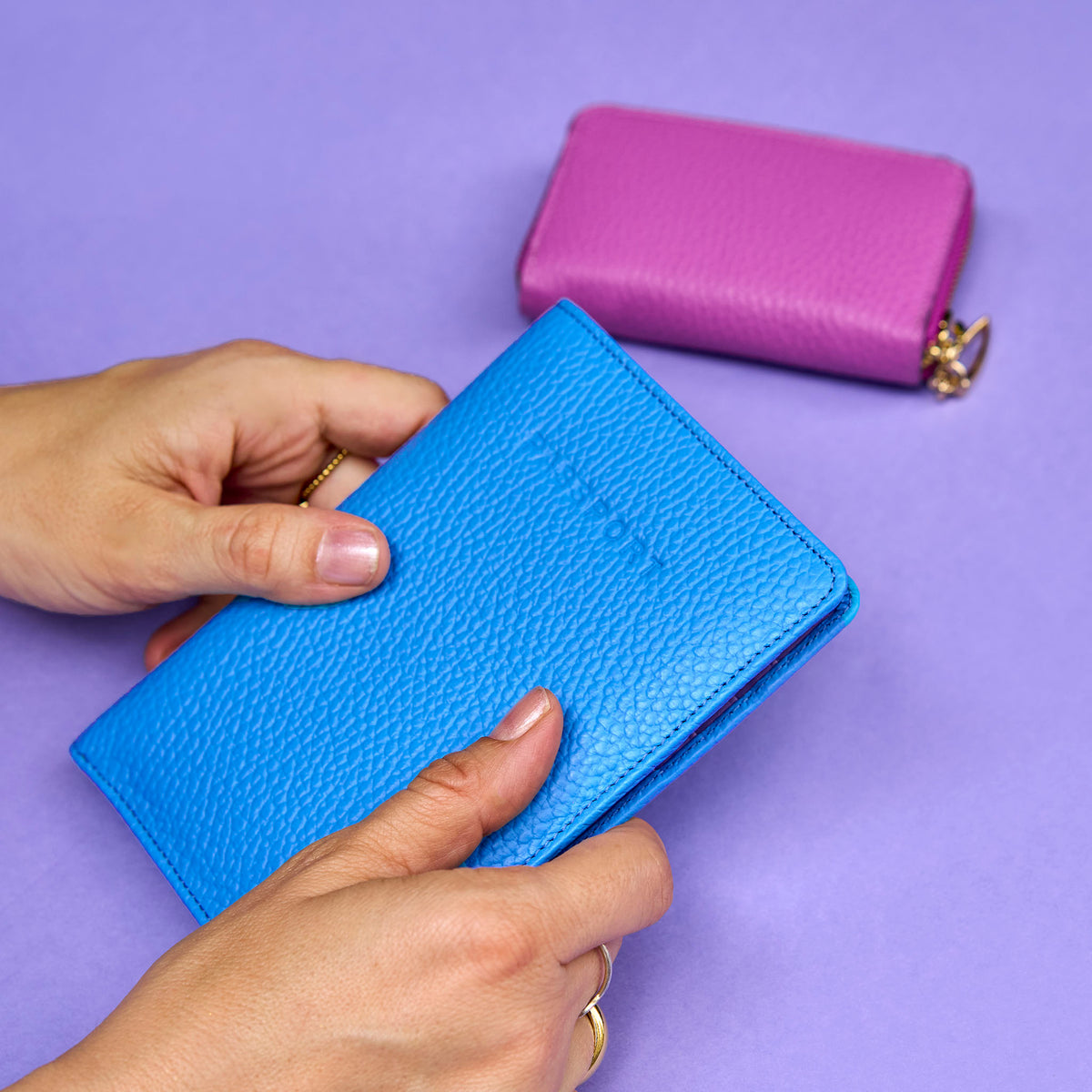 Blue leather wallet held by a hand with a purple background - AZURE