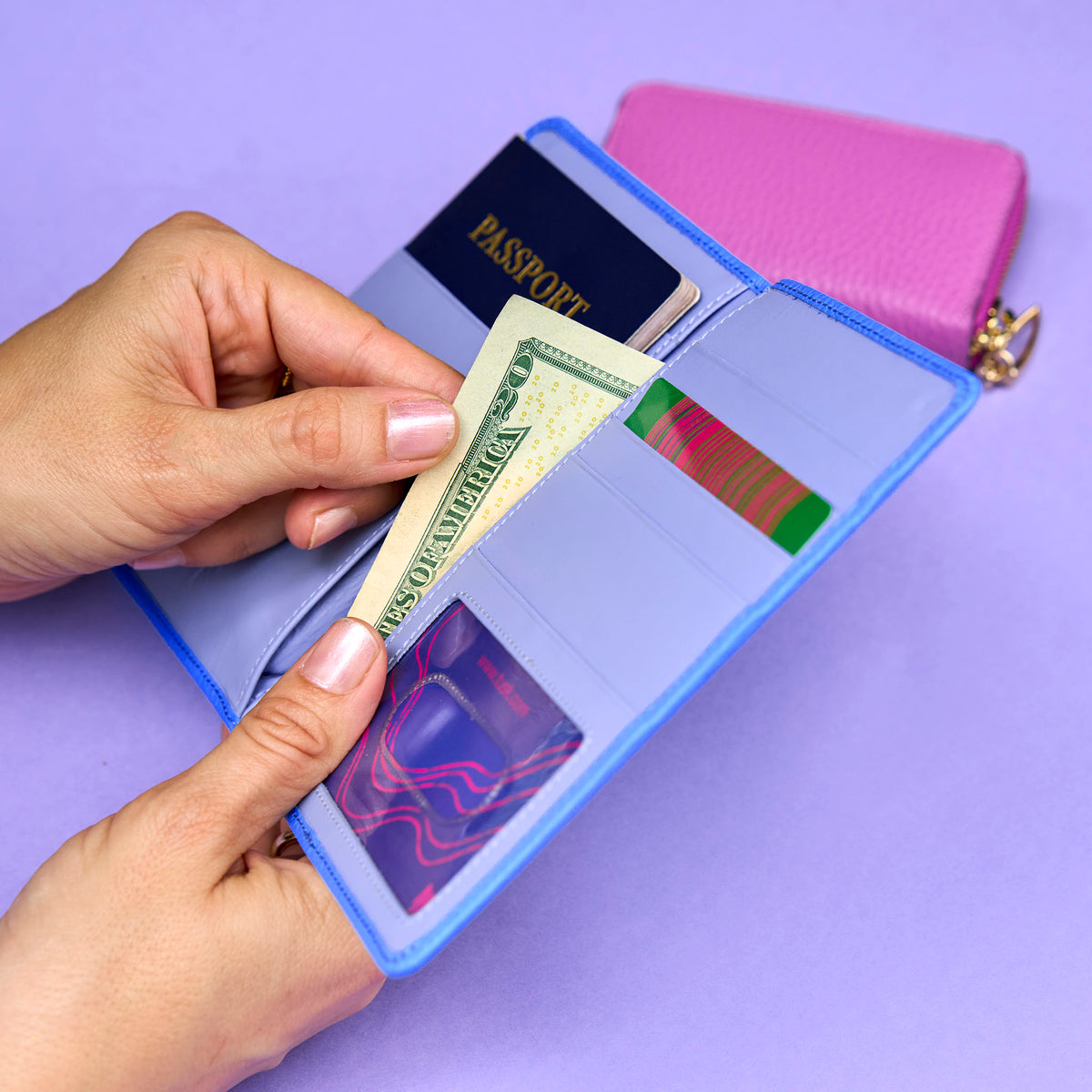 Person holding a dollar bill over an open blue passport wallett with a passport and other documents on a purple background - AZURE