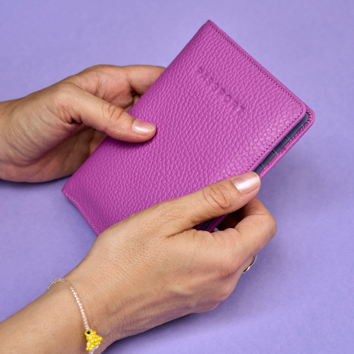 Mgenta passport wallet held by hands on a purple background - MAGENTA