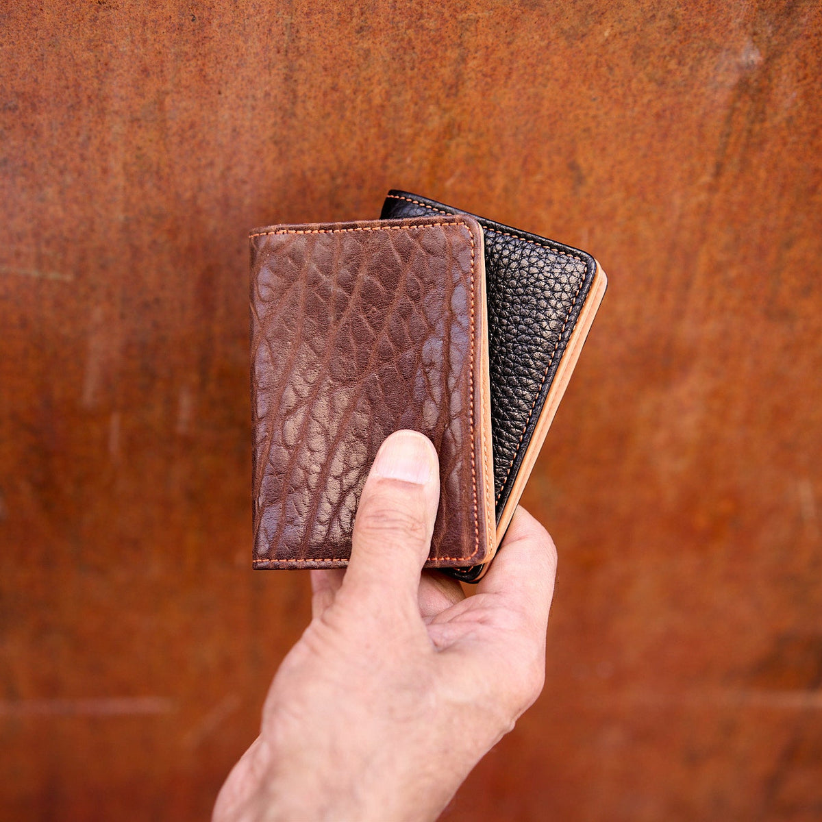 Man holding two  pebble grain leather card cases - CHOCOLATE