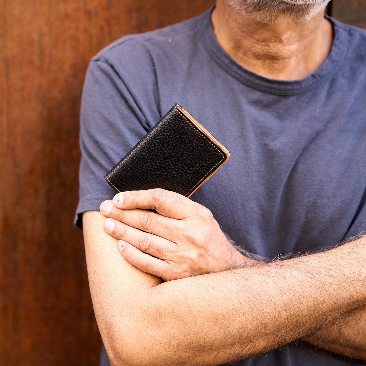 Man with folded arms holding black pebble grain leather card case - BLACK