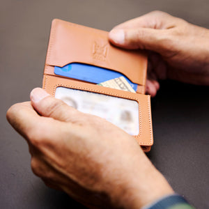 Person holding a brown leather wallet with cards and money on a dark background - TAN