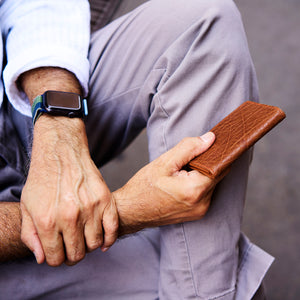 Person holding a brown leather wallet with a blurred background - TAN