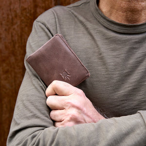 Person holding a brown leather wallet with a visible brand logo - BROWN