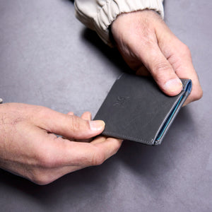 Person holding a black leather wallet on a gray surface - GREY