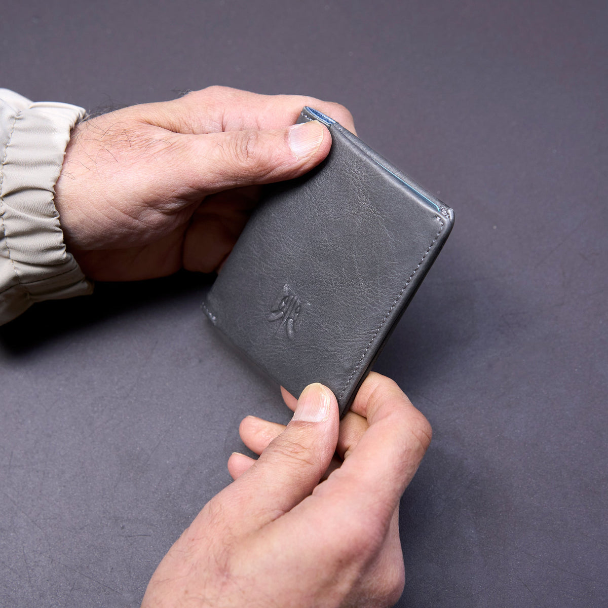 Person holding a black leather wallet against a gray background - GREY