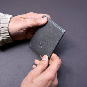 Person holding a black leather wallet against a gray background - GREY