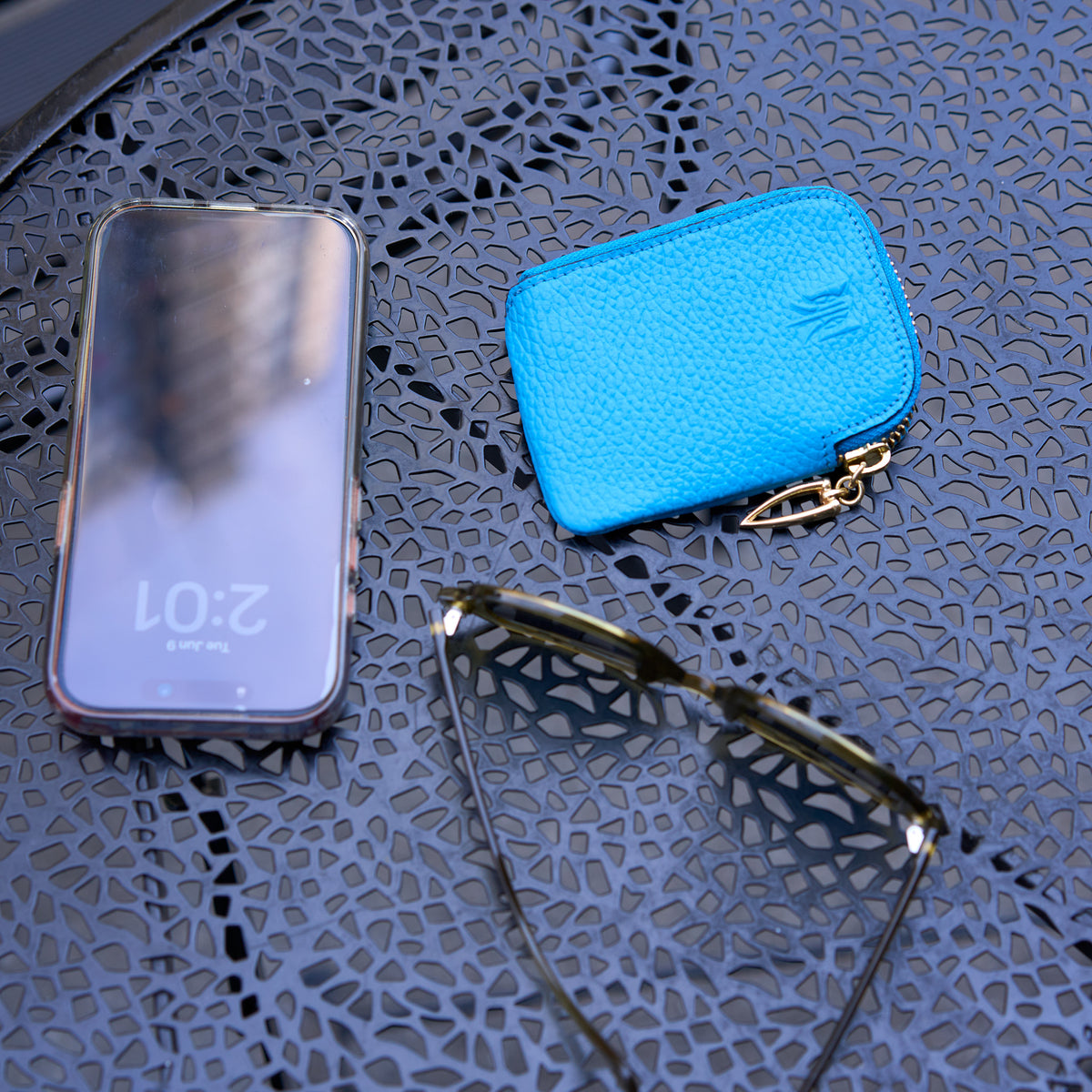 Tusk 194 Ascot small zip card wallet, beside a phone and sunglasses on a cafe table - AZURE