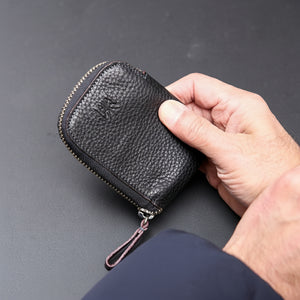 Hand holding a black textured wallet on a gray background - BLACK