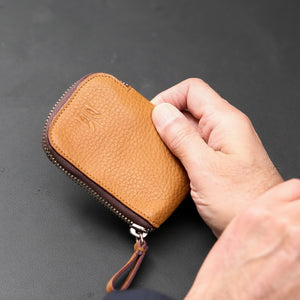 Hand holding a brown leather wallet against a dark background - TAN