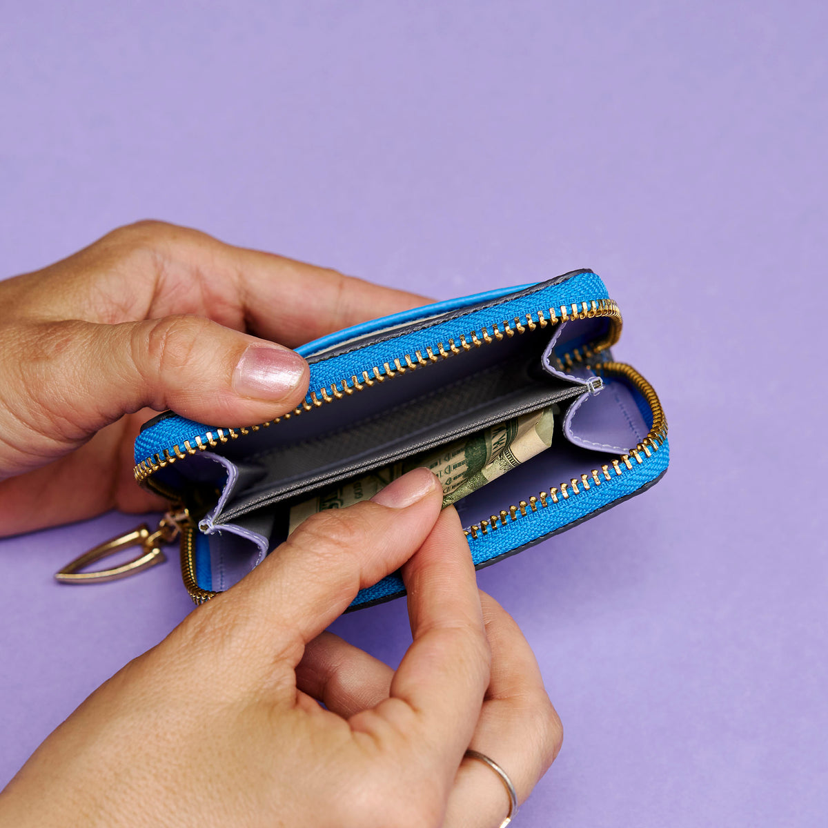 Blue leather wallet with gold zipper being held open against a purple background - AZURE