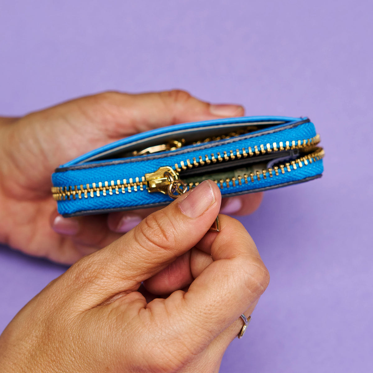Blue leather wallet with gold zipper held by a hand against a purple background -AZURE