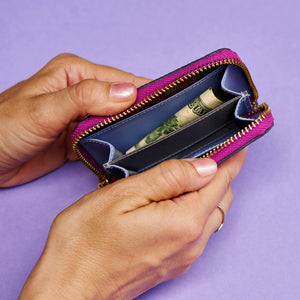 Person holding an open magenta leather wallet with money against a purple background - MAGENTA