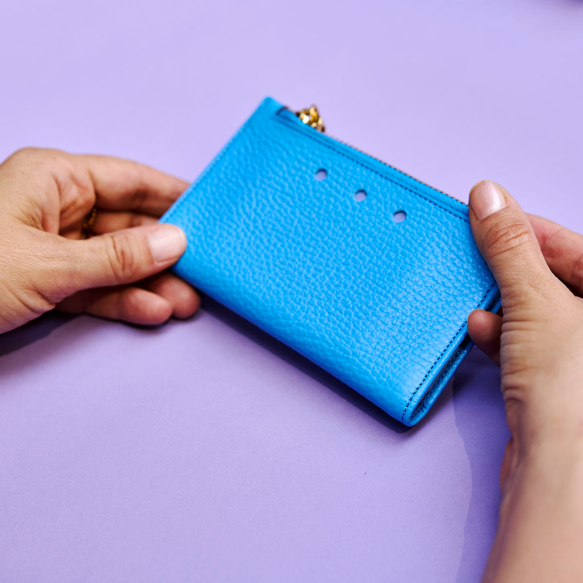 Blue wallet held by two hands against a purple background - AZURE