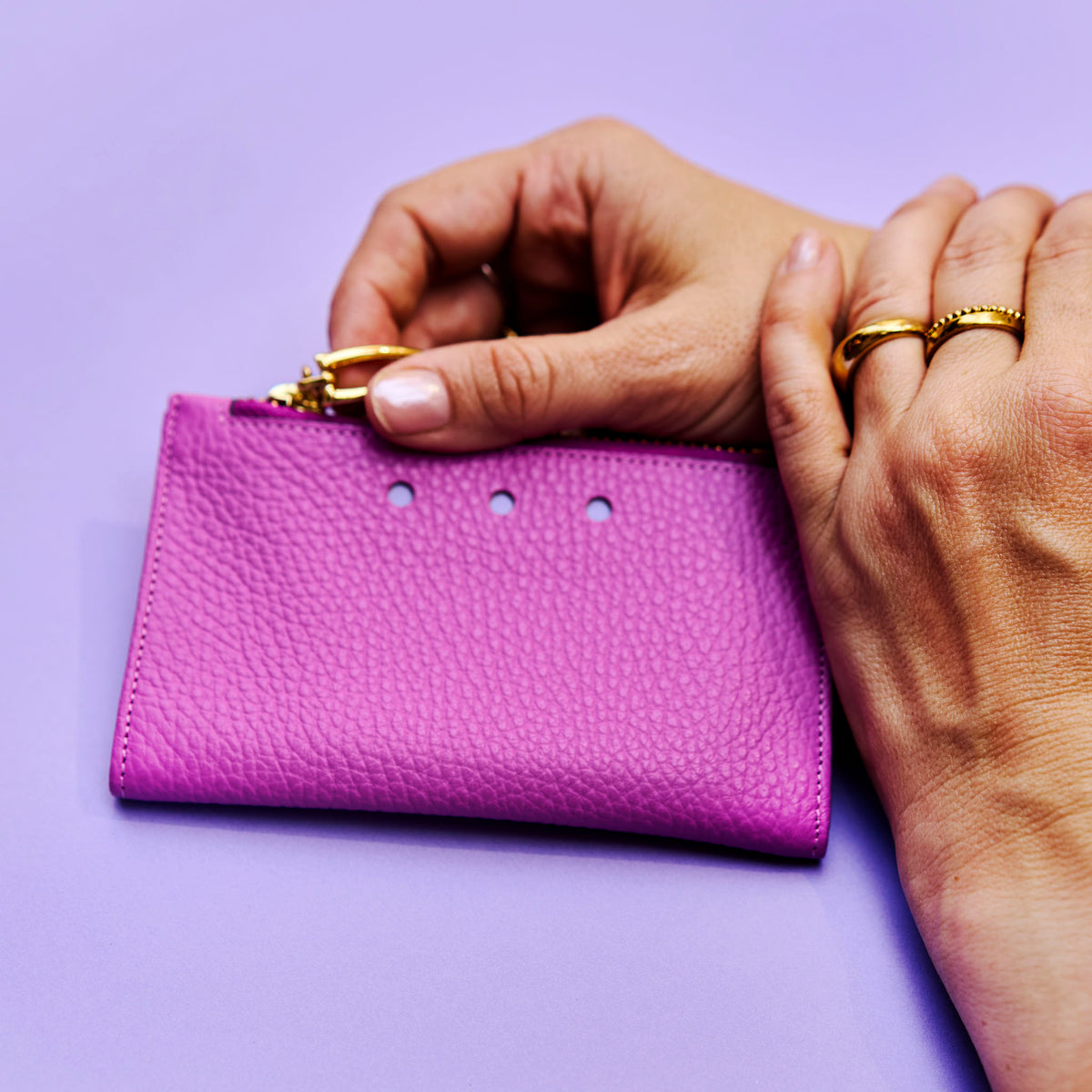 Magenta leather wallet held by hands with gold rings on a purple background - MAGENTA