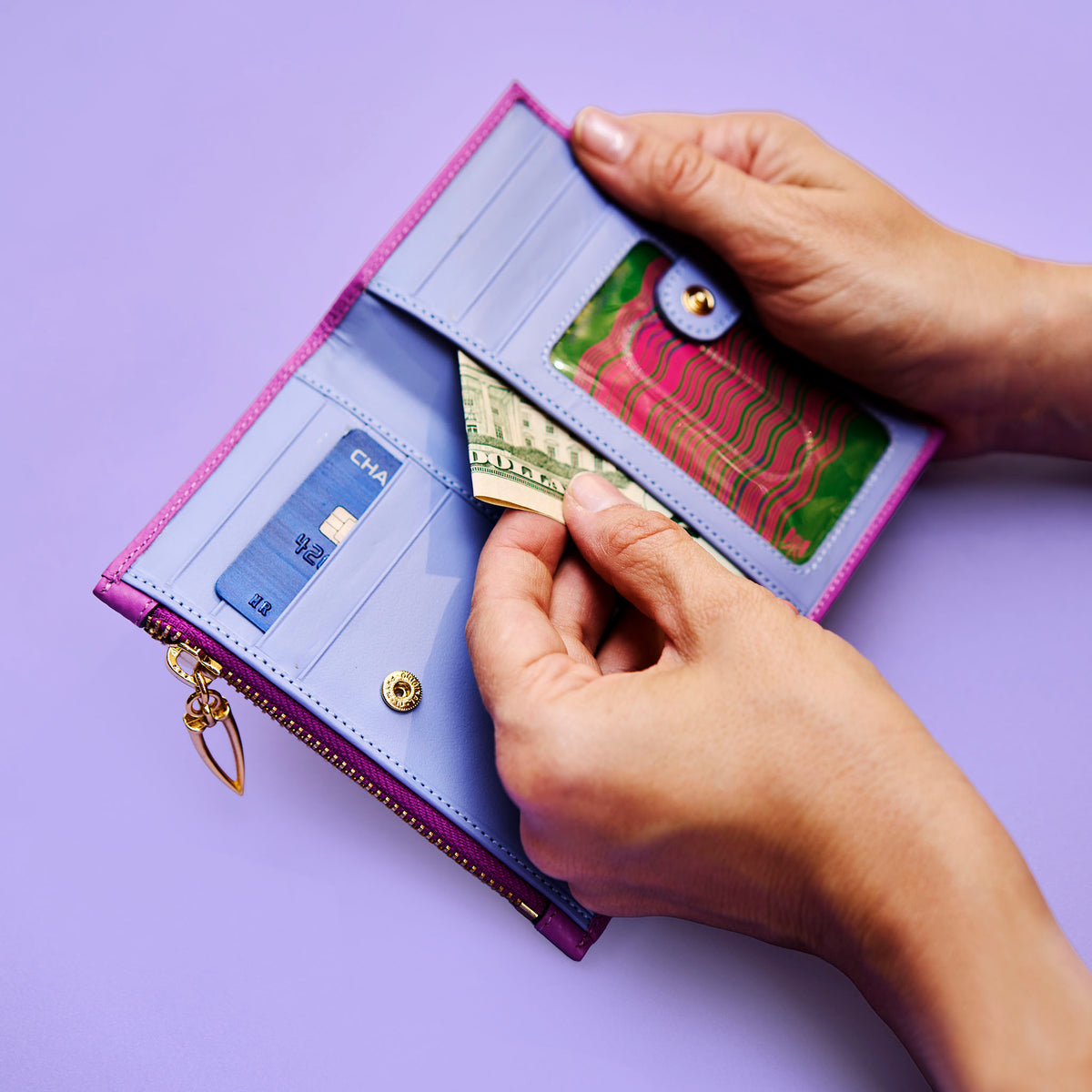 Hand holding an open magenta leather wallet with cards on a purple background - MAGENTA