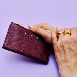Hand holding a maroon leather wallet against a purple background - OXBLOOD