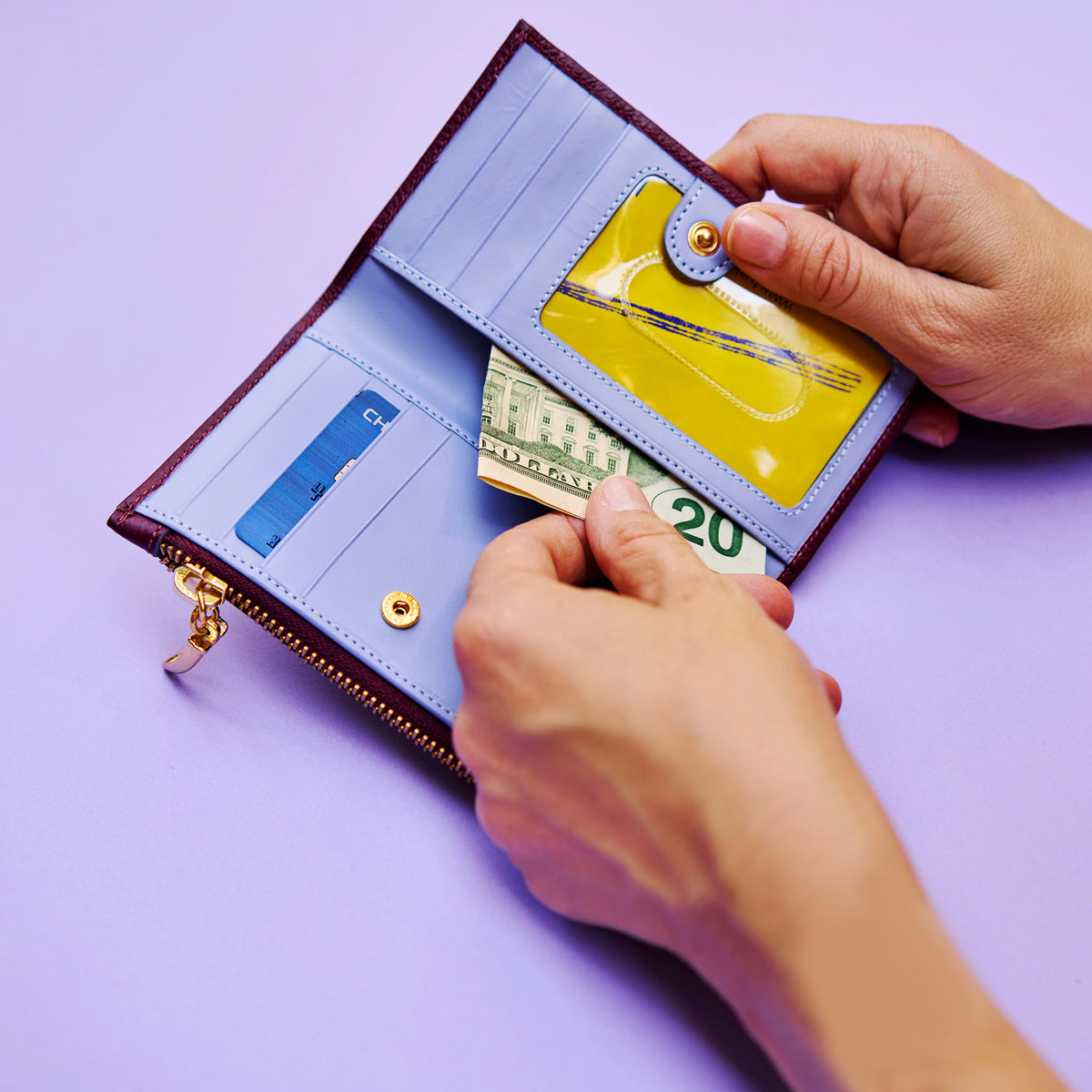 Person opening a maroon wallet on a light purple background - oxblood