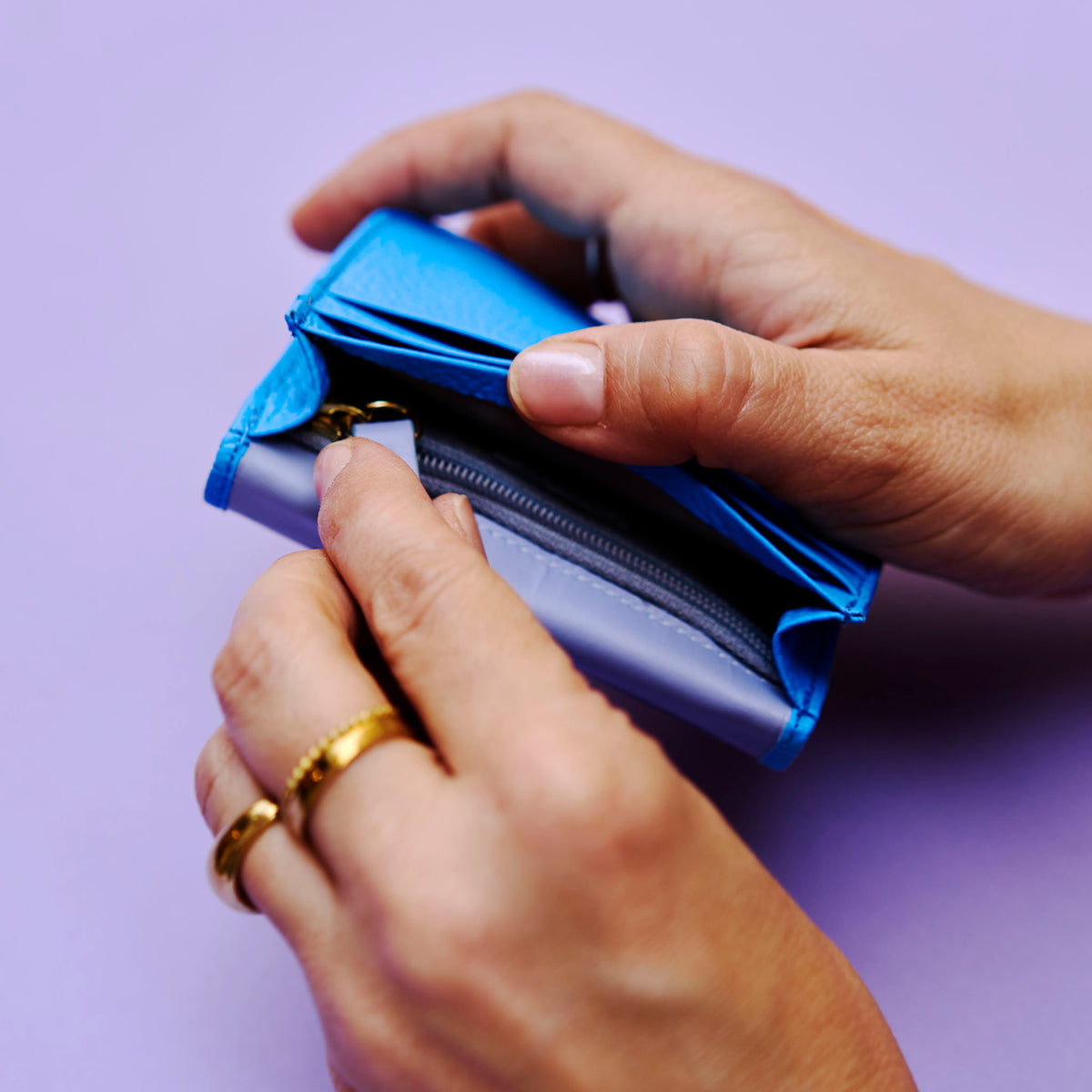 Close-up of hands opening a blue leather wallet against a purple background - AZURE