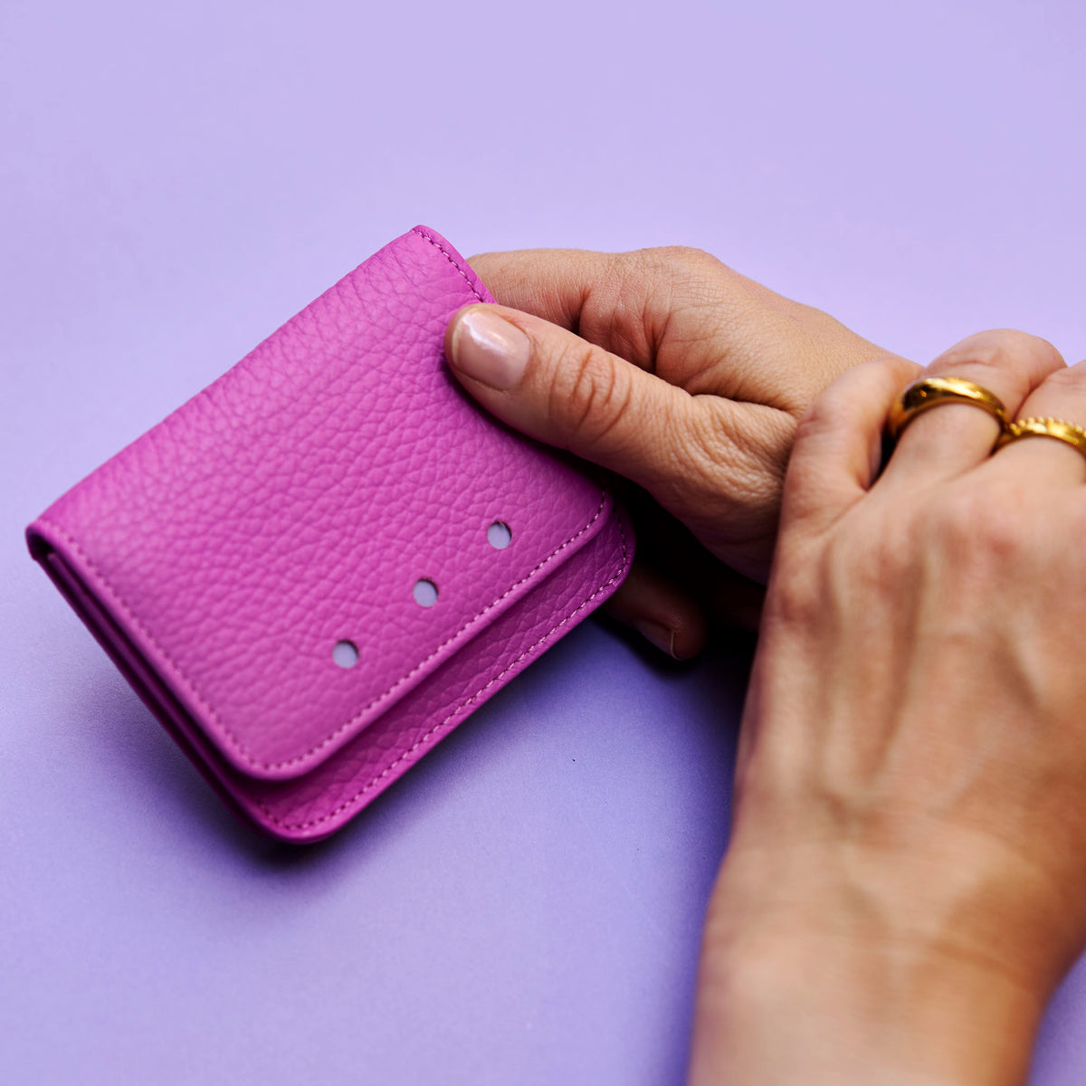 Hand holding a magenta leather wallet against a purple background - MAGENTA