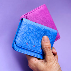 Hand holding a blue and magenta leather wallet against a purple background - AZURE