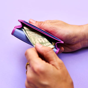 Hand holding a magenta leather wallet with money against a light purple background - MAGENTA