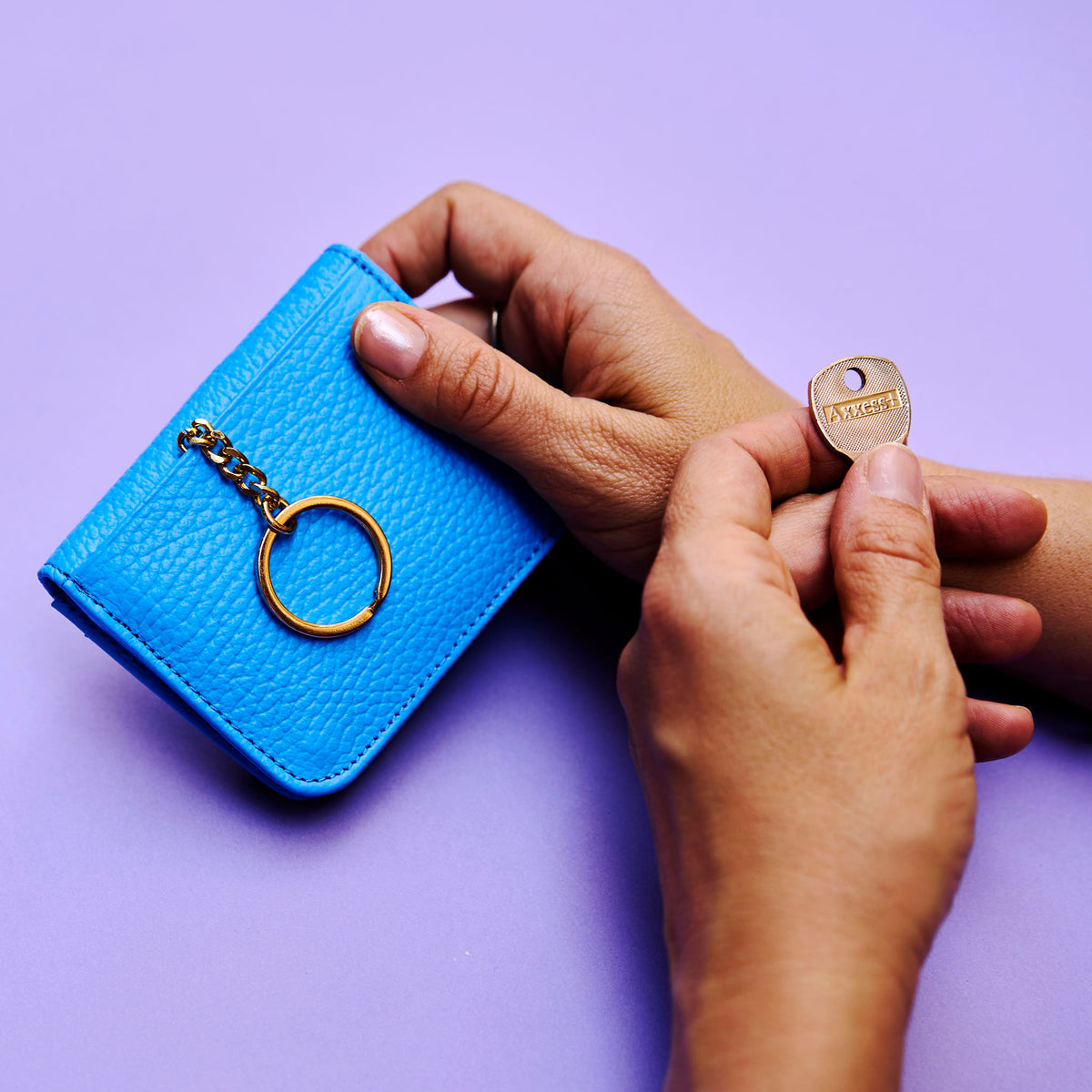 Blue leather wallet with a keychain held by hands on a purple background - AZURE