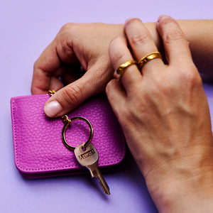 Magenta  leather wallet with a key and keychain on a purple background - MAGENTA
