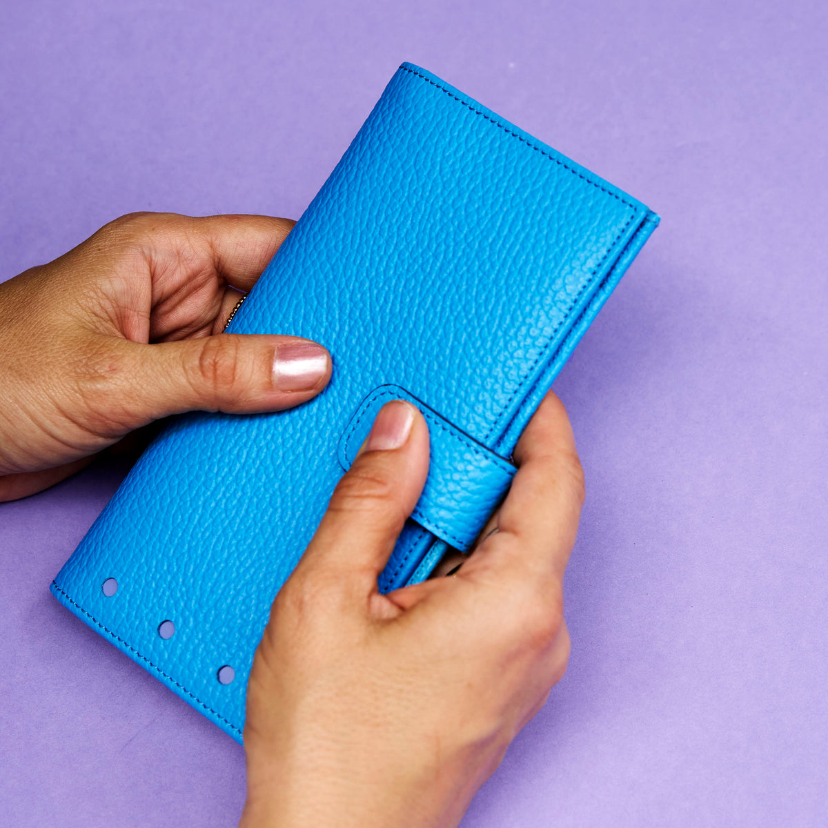 Blue wallet held by hands against a purple background - AZURE