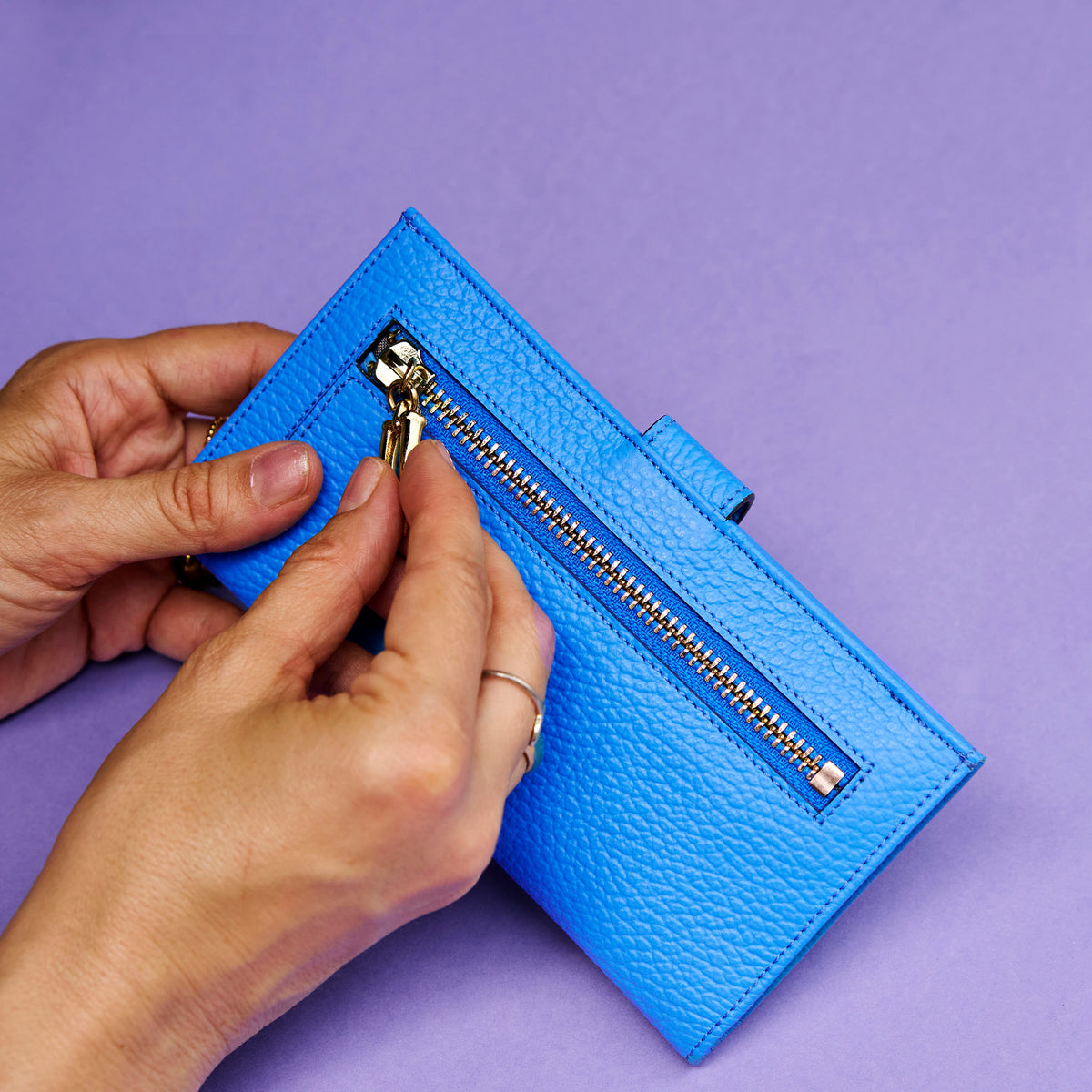 Blue wallet with gold zipper being held against a purple background - AZURE