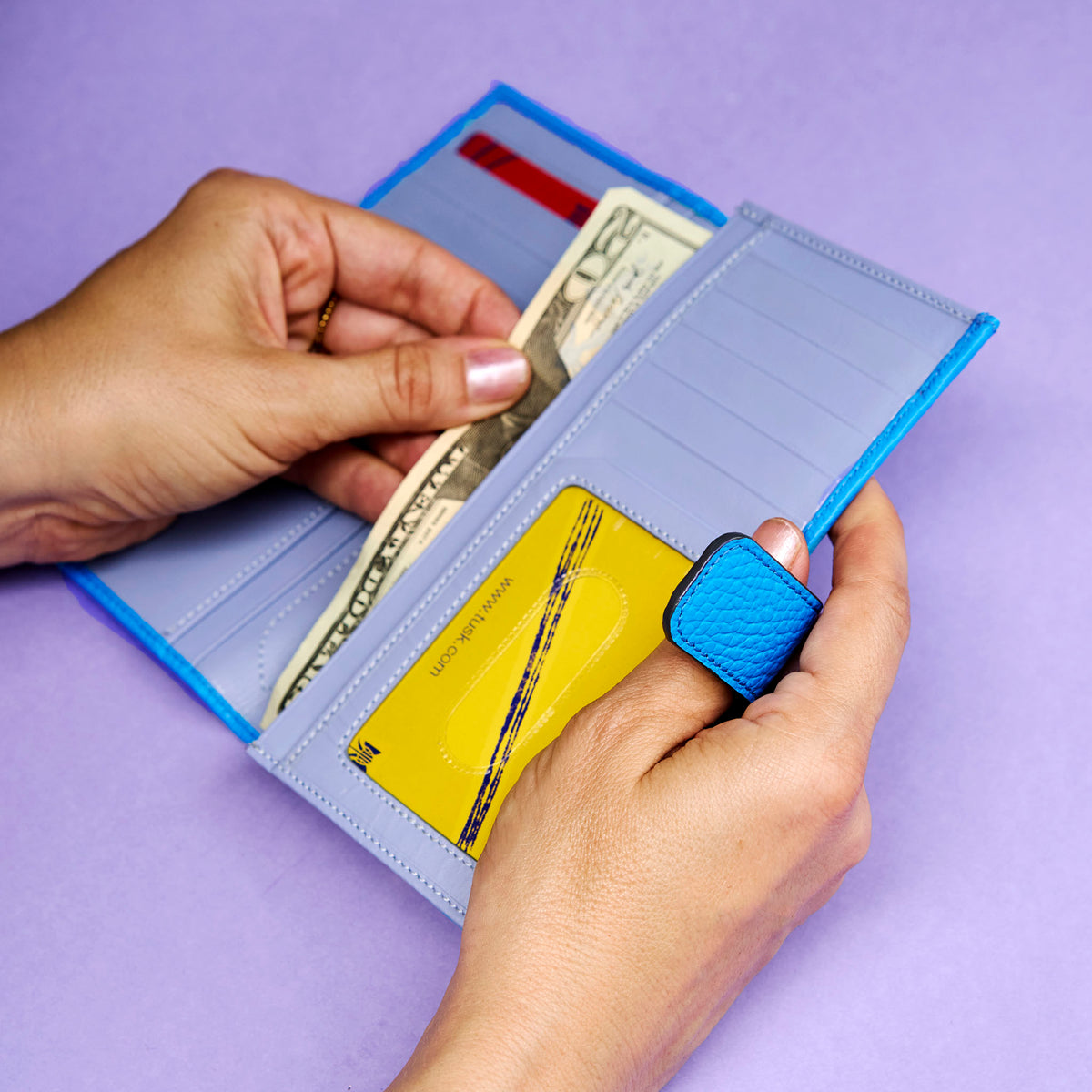 Person holding a blue wallet with money and cards on a purple background - AZURE