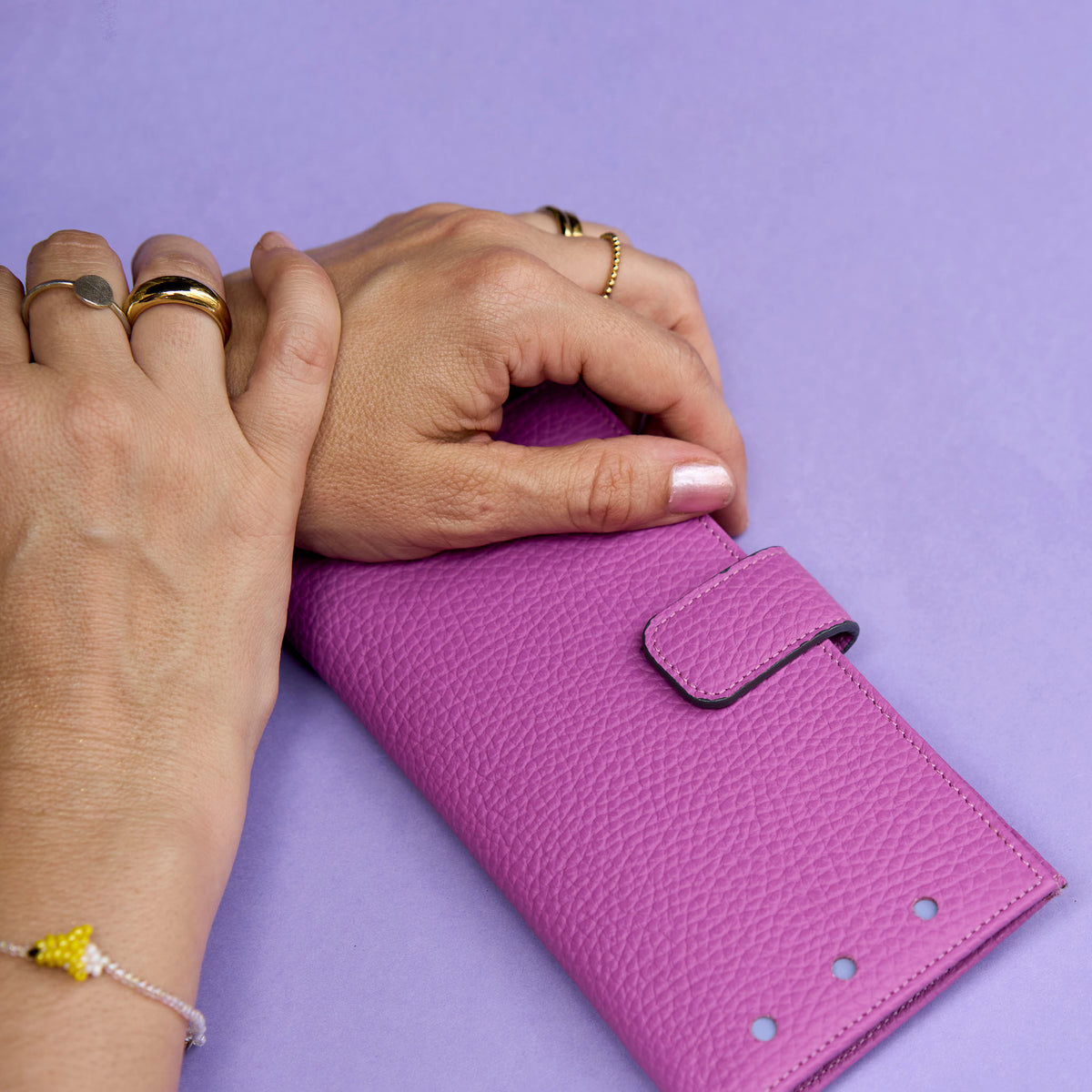Magenta wallet held by two hands on a purple background - MAGENTA